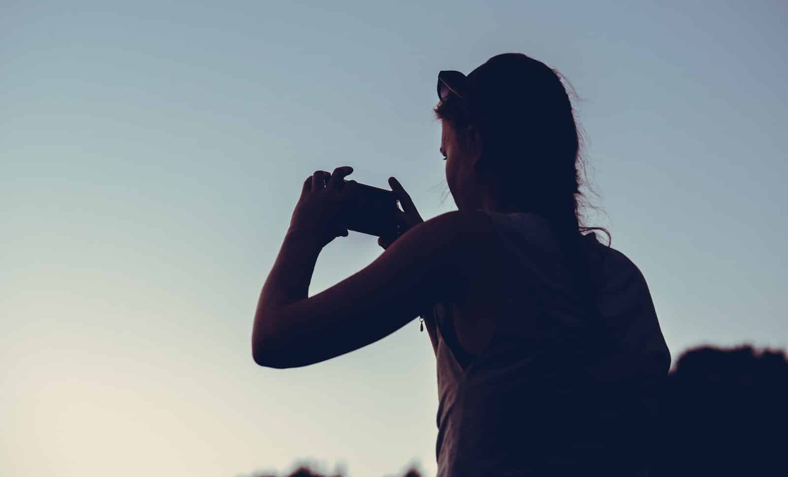 silhouette of woman taking photo of sunrise